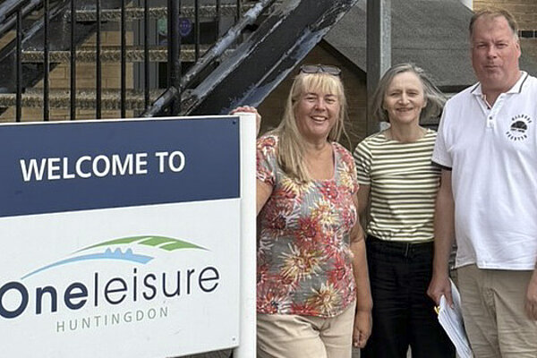 Cllrs Lou Ascroft, Ann Blackwell, and Tom Sanderson standing by a OneLeisure Huntingdon sign