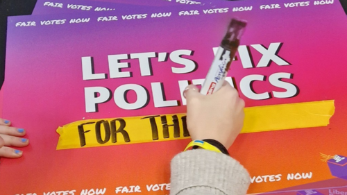 A poster reading "Let's Fix Politics", with someone in the process of writing "For Our NHS" underneath it