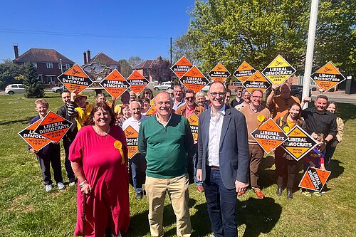 Ed Davey with Liberal Democrat activists holding orange diamond placards
