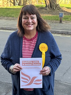 Cllr Sarah Conboy holding a copy of the 2026 HDC LDs manifesto, and wearing a yellow LD rosette