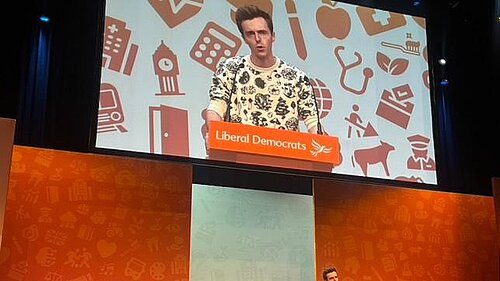 Cllr Nathan Hunt speaking on a Liberal Democrat branded stage